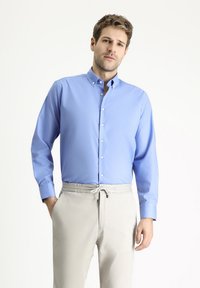 Camisa azul claro con botones y mangas largas, de textura suave y con collar, combinada con pantalones grises claros de cintura elástica.