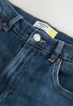 Közepes derékú slim farmernadrág sötétkék denimből. Gombos záródással, sárga címkével és diszkrét varrási részletekkel rendelkezik.