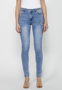 Skinny jeans in light blue denim, featuring a smooth texture, subtle fading, and floral embroidery on the left thigh.