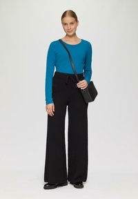 Turquoise lange mouwen top gecombineerd met hoge taille zwarte wijde broek. Voorzien van een koord in de taille en biedt een ontspannen pasvorm. Zwarte crossbodytas inbegrepen.