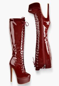 Bottes rouge en cuir verni montant jusqu'au genou avec un laçage à l'avant, des fermetures éclair latérales et un talon aigu élevé. Dotées d'une semelle plateforme pour plus de hauteur.