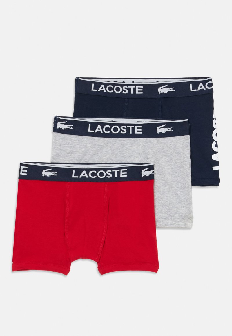 Três pares de boxers Lacoste nas cores vermelho, cinza e azul-marinho. Cada par apresenta uma cinta com a marca em um design contrastante. Material em algodão.