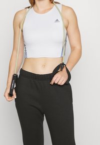 Vit sportig crop top med blå detaljer, i kombination med svarta mjukisbyxor. En hopprep hålls i ena handen, vilket visar upp en sportig outfit.