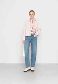 Svijetlo ružičasta skraćena jakna preko turtlenecka s uzorkom crvenih srca. Visoki traperice u plavoj boji i svijetlo ružičaste cipele upotpunjuju outfit.