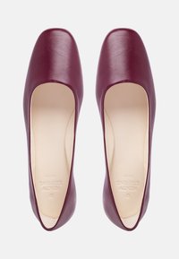 Burgundy leather pointy-toed flats with a smooth texture and minimalistic design, featuring an open side cut and a beige interior.