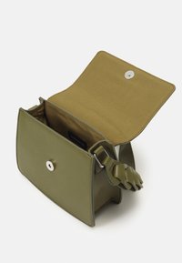 Kwadratowa oliwkowa torba na ramię z otwartą klapą, zapięciem na magnes, pojedynczą komorą i szczegółową plecionką rączki na białym tle.