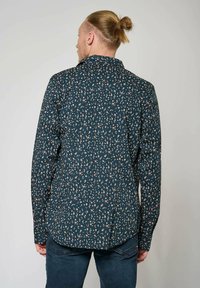 Shirt met een donkerblauwe achtergrond en kleine, verspreide bloemmotieven in roze en crème. Lange mouwen, button-down kraag en een gebogen onderkant.