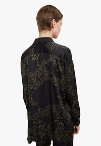 Camicia di seta nera con vestibilità morbida, caratterizzata da un motivo astratto dorato, colletto classico, dettagli di cuciture visibili e maniche lunghe.