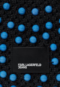 Fekete szőtt textil fényes kék műgyöngyökkel, amelyen egy fekete téglalap alakú címke található, rajta fehér betűkkel a "KARL LAGERFELD JEANS" felirattal.