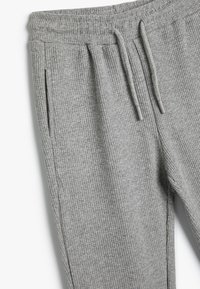 Pantalones de chándal grises acanalados con cinturilla elástica, cierres de cordón y bolsillos laterales. La tela texturizada proporciona una apariencia acogedora.