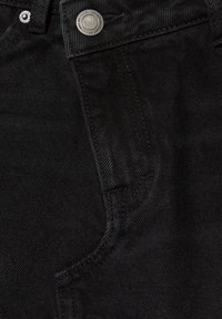 Gros plan sur un jean en denim noir montrant la poche avant et un bouton métallique avec un logo gravé.
