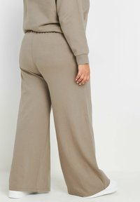 Ljusbruna vide byxor i mjukt tyg med elastisk midja, med en avslappnad passform och vita ankeldetaljer.