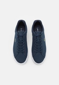 Marine lerretsneakers med hvite gummisåler. Egenskaper inkluderer rund tå, snøring og Lacoste-rolig logo på siden.