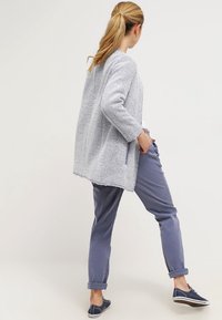 Ljusblå texturerad cardigan med trekvart ärmar, kombinerad med ljusgrå byxor och marinblå sneakers. Öppen ryggdesign med sidofickor.