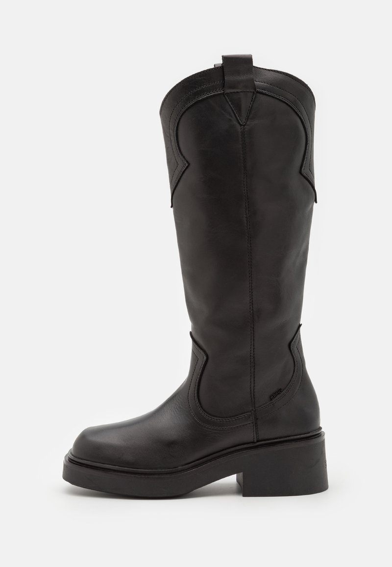 Botte haute en cuir noir avec bout arrondi, coutures décoratives, languette en haut et talon bloc épais sur fond blanc.
