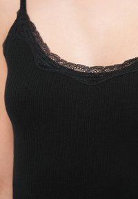 Μαύρο ριμπ αμάνικο τοπ με δαντελωτή διακόσμηση κατά μήκος του λαιμού, τονίζοντας την υφή και το σχέδιο χωρίς επιπλέον στολίδια.