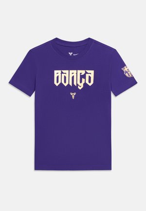 T-shirt violet à manches courtes avec « BARÇA » en police beige stylisée sur le devant, logo de Kobe Bryant en dessous, et écusson du FC Barcelone sur la manche droite.