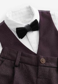 Burgundy színű mellény és mintás nadrág fehér, galléros inggel és fekete bársonyból készült csokornyakkendővel párosítva. Gomb részlet látható.