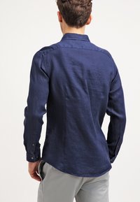 Mörk marinblå långärmad skjorta i lätt linnetyg, med en knapp-down krage och manschetter, samt en något rundad nederkant.
