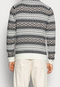 Neulepaita, jossa on musta, ruskea ja valkoinen geometrinen kuvio. Resorireunaiset hihansuut ja helma. Rento istuvuus, pitkät hihat.