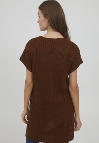 Pull oversized en maille marron avec des manches courtes, présentant un motif texturé et un décolleté large, atteignant la mi-cuisse.