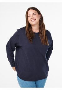 Teemansinist pusa pehmest kangast, ümar kaelus, pikad varrukad ja lõdvestunud lõige, kombineeritudhele sinise teksaga.