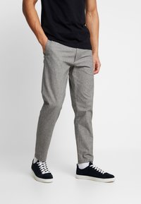 Pantalon à carreaux gris à coupe slim, avec des poches en biais, associé à des baskets bleu marine et un t-shirt noir ajusté.