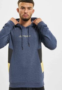 Sudadera con capucha en azul marino con un acabado texturizado. Presenta un diseño a rayas amarillas y negras; cordones y logo bordado.