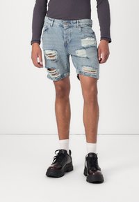 Ljusblå slitna denimshorts med flera revor, fransiga fållar och fem fickor, kombinerat med svarta snörskor och vita strumpor.