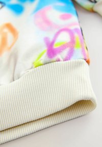 Polarowy sweatshirt z kolorowym wzorem graficznym w odcieniach różowego, niebieskiego i zielonego. Prążkowane białe mankiety o strukturalnym wykończeniu.