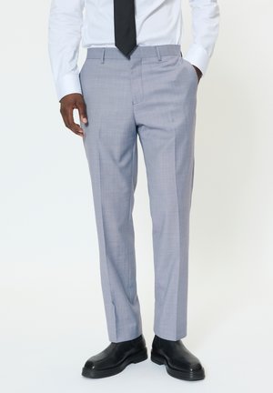 Lysegrå skræddersyede bukser med et diskret ternet mønster, flad front, sidelommer og en slank pasform, båret med sorte sko.