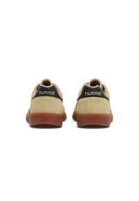 Sneakers in suede beige con accenti scuri, suola in gomma, forma arrotondata e dettaglio di cucitura visibile. Nome del marchio "hummel" sul tallone.