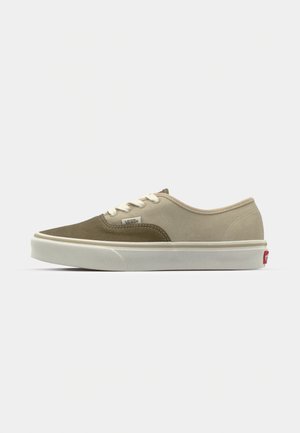 Bruna och beige kanvasskor med vit sula och snören. Har en Vans-logotyp och en röd detalj på hälen. Lågskuren design.