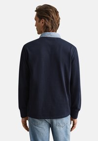 Marineblauw shirt met lange mouwen en een contrasterende licht denimkraag, met een ontspannen pasvorm en zachte textuur, gezien vanaf de achterkant.