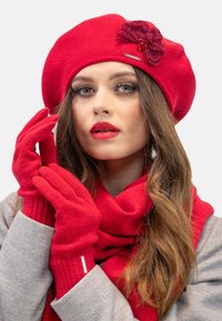 Béret tricoté rouge avec une fleur décorative, gants en tricot rouge assortis et une écharpe rouge. Texture douce avec des accents côtelés.