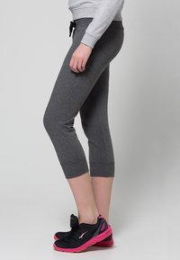 Pantalones de chándal capri grises, hechos de un material suave y con un diseño ajustado, que cuentan con una cintura elástica con cordón y dobladillos recortados. Combinados con zapatillas negras y rosas.