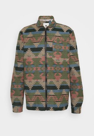 Chaqueta de manga larga con cierre de cremallera y cuello alto, que presenta patrones geométricos tribales en tonos verdes, rosa, beige, azul y negro.