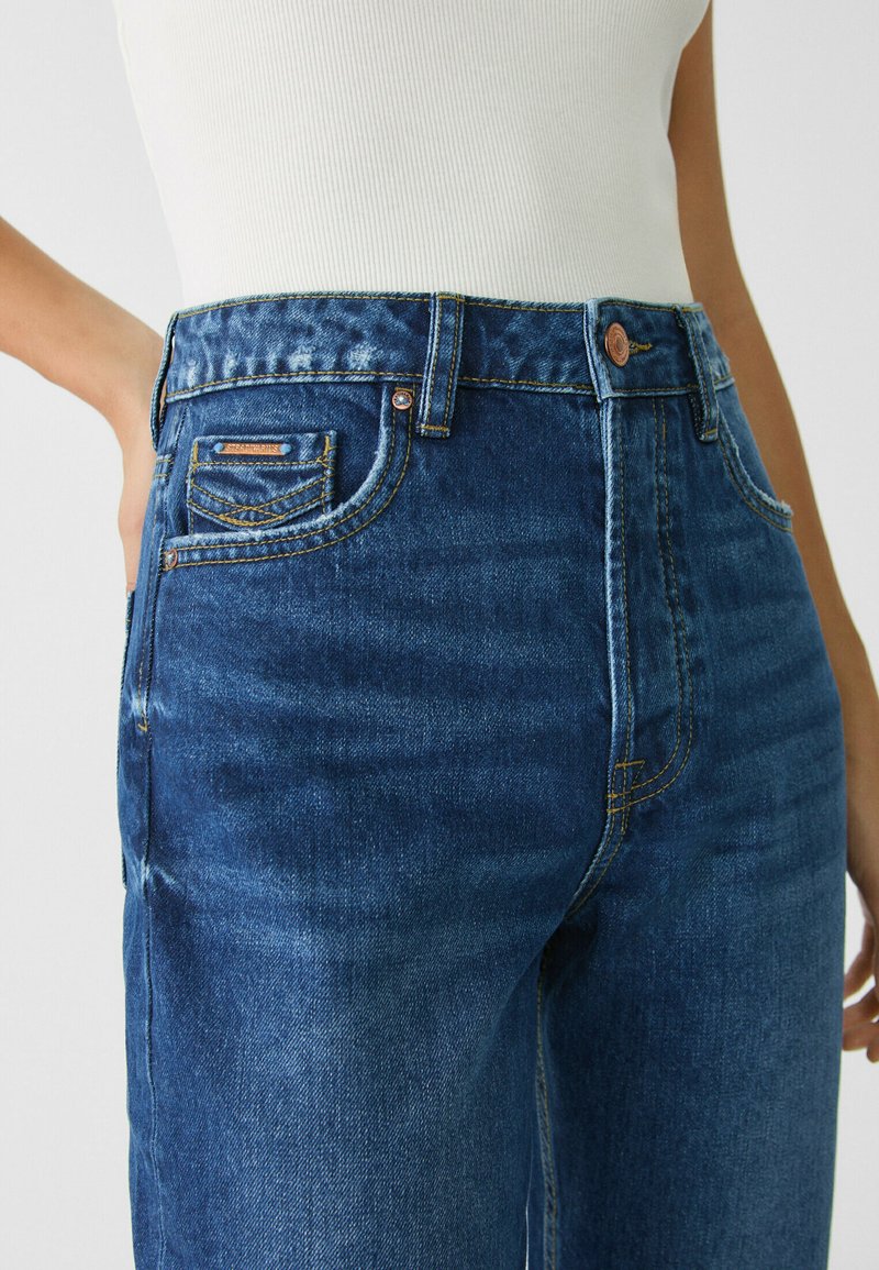 Hochtaillierte Denim-Jeans in Dunkelblau, mit glatter Textur, Kupferknopf und dezenten, ausgewaschenen Akzenten, sowie Fronttaschendetails.