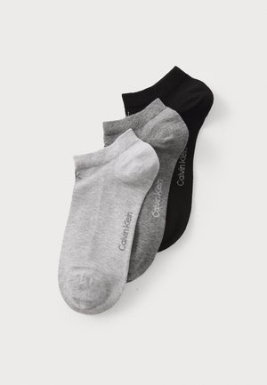 Trois paires de chaussettes de cheville : une noire, une gris foncé, une gris clair. Fabriquées en tissu doux avec un orteil sans couture et un logo Calvin Klein.