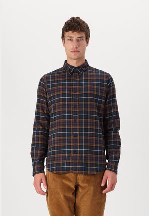 Camicia a quadri blu navy con accenti arancioni e bianchi, con colletto, maniche lunghe e vestibilità comoda. Indossata con pantaloni in velluto a coste color beige.