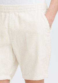 Kremfargede kordfløyelsshorts med vertikal ribbing, sidelommer og elastisk liv. myk tekstur, kne-lengde kutting.