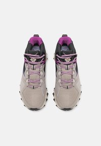 Lekki obuwie turystyczne w beżowym kolorze z czarnymi i purpurowymi akcentami. Siatkowa cholewka, gumowa podeszwa i zabezpieczone sznurowadła. Teksturowana powierzchnia dla lepszej przyczepności.
