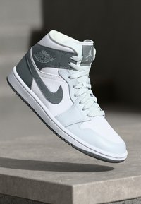 Baskets Air Jordan avec une tige en cuir blanc et des accents gris clair, design mi-haut et semelle en caoutchouc noire avec texture imprimée.