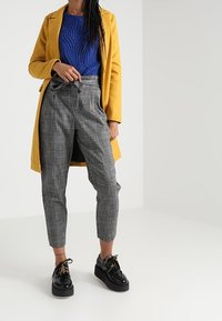 Keltainen takki, sininen teksturoitu neulepaita, harmaat ruutuhousut, mustat korokkeella varustetut kengät, joissa on kultaisia yksityiskohtia. Rentoa asustusta kerroksittain.