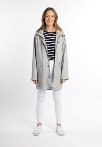 Giacca impermeabile grigio chiaro con cappuccio, zip frontale e bottoni a pressione. Presenta due tasche laterali e una vestibilità comoda. Sotto, una maglietta a righe.