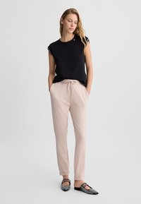 Schwarzes, kurzärmeliges Oberteil mit Spitzenakzenten, beige Hosen mit elastischem Bund und schwarze Ballerinas mit Nieten; glatte Stoffe und lockere Passform.