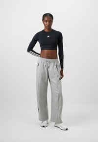 Crop top nero a maniche lunghe con tre strisce bianche e pantaloni della tuta larghi grigi con tasche laterali e dettagli neri.