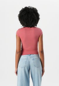 Smal tilpasset t-skjorte med korte ermer i støvet rosa, laget av myk, elastisk stoff. Kombinert med lyseblå vide jeans med baklommer.