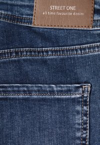 Tmavě modrá džínovina s koženou visačkou označenou "Street One" a bílým textem. Má zadní kapsu s viditelným prošitím.
