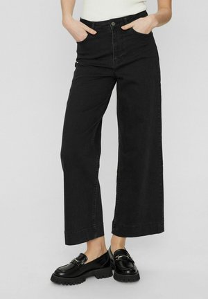 Breda svarta denimjeans med hög midja, framfickor och knappgylf. Matchat med kraftiga svarta loafers. Slät textur.